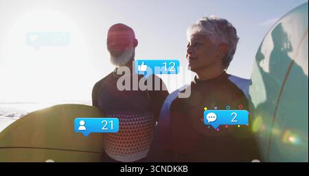 Couple de surfeurs debout portant des combinaisons tenant des planches de surf plage au lever du soleil, avec des icônes flottantes Banque D'Images