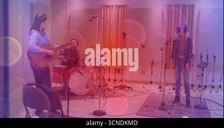 Trois musiciens enregistrant la chanson en studio, portant des écouteurs avec guitare acoustique et kit de batterie rouge Banque D'Images