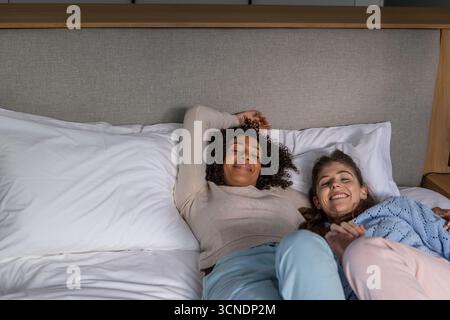 Diverses amies féminines allongées côte à côte sur le lit dans la chambre avec tête de lit grise Banque D'Images