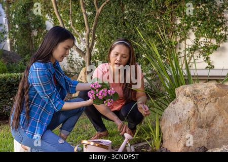 Mère asiatique et fille agenouillant la plante à fleurs à côté de l'arrosage dans la cour arrière Banque D'Images