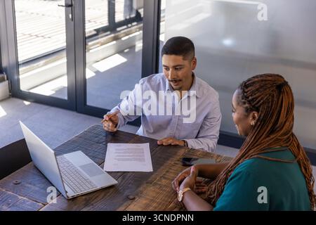 Divers collègues examinant les détails du projet à la table de conférence de bureau avec ordinateur portable, document Banque D'Images