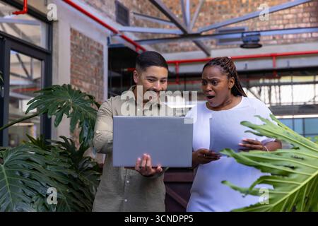 Divers collègues examinant l'ordinateur portable et examinant les documents imprimés, les plantes tropicales dans le bureau Banque D'Images
