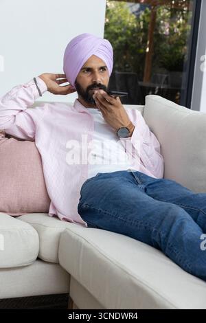 Homme indien utilisant un smartphone tout en étant assis sur un canapé dans le salon Banque D'Images