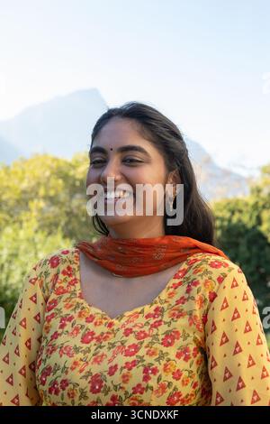 Femme indienne debout dans le parc portant kurta jaune, dupatta orange, boucles d'oreilles, goujon de nez Banque D'Images