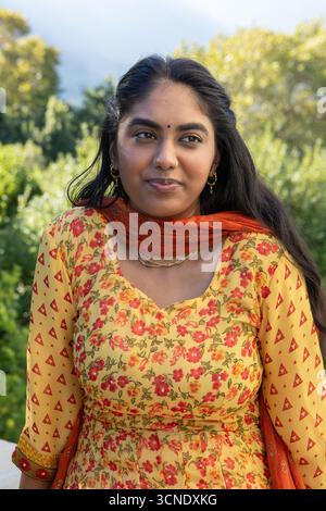 Femme indienne debout dans le parc portant kurta avec dupatta orange et bijoux en or avec bindi Banque D'Images