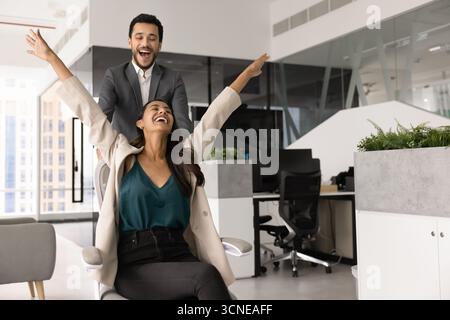 Couple de jeunes collègues chevauchant la chaise de bureau dans l'espace de travail Banque D'Images