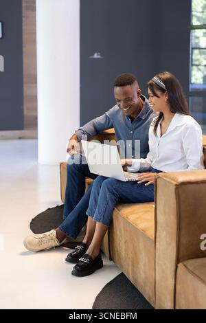 Divers collègues collaborant sur un ordinateur portable, assis sur un canapé en cuir sur un tapis noir au salon de bureau Banque D'Images