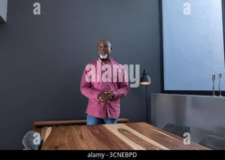 Homme afro-américain senior debout derrière la table de conférence dans le bureau portant une chemise Banque D'Images