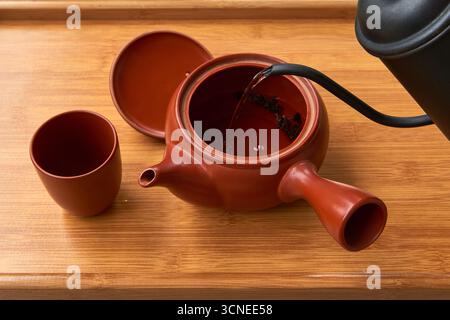 Le processus de brassage du thé, avec de l'eau chaude versée dans une théière d'argile traditionnelle remplie de feuilles de thé. Un concept pour une cérémonie du thé, un matin Banque D'Images