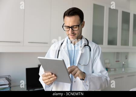 Le médecin masculin souriant communique avec le patient par chat en utilisant la tablette Banque D'Images