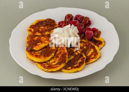 Les crêpes moelleuses sont empilées sur une assiette blanche, surmontées de crème fouettée et arrosées de sauce caramel, aux côtés de framboises fraîches pour une pause sucrée Banque D'Images