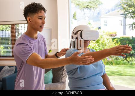 Instructeur diversifié guidant le participant senior à l'aide d'un casque VR dans le salon par canapé, espace de copie Banque D'Images