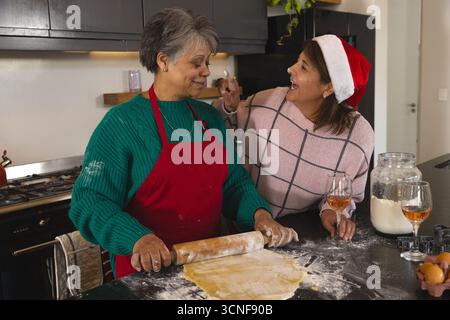 Mère et fille diversifiées faisant cuire sur le comptoir de cuisine en utilisant un rouleau à pâtisserie en bois et des emporte-pièces Banque D'Images