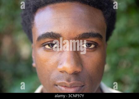 Homme afro-américain posant pour la prise de vue de portrait dans le parc en chemise à col avec fond de feuillage Banque D'Images
