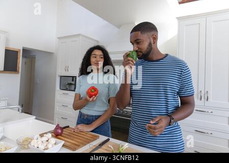 Couple diversifié tranchant le poivron vert, le poivron rouge sur la planche à découper à l'îlot de cuisine Banque D'Images