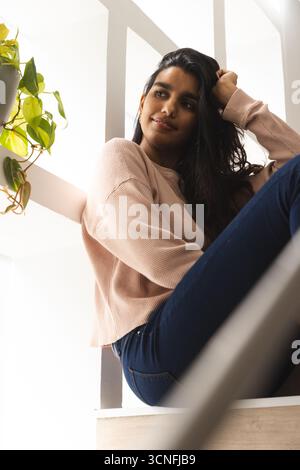 Femme asiatique appuyée contre des poutres sur un palier d'escalier peint en blanc à côté d'une plante de vigne suspendue Banque D'Images