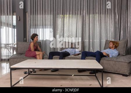 Divers amis se relaxant sur le canapé sectionnel gris dans le salon avec table basse en bois Banque D'Images