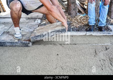 Installation d'une nouvelle chaussée ou d'un nouveau plancher à l'extérieur de grands carreaux de béton, détail de la fermeture sur un travailleur masculin qui pose un bloc de pierre sur une couche de base de sable et de gravier Banque D'Images