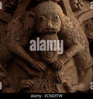 Deux lions partageant une tête dévorent l'homme des cheveux vers le bas : capitale sculptée du XIIe siècle après JC dans le portail d'entrée de l'hôpital monastique bénédictin ou hospice de Saint-Julien l'hospitalier, construit à Besalú, ancienne ville catalane dans la province de Gérone, Espagne, pour offrir hébergement et nourriture aux pèlerins suivant le Camino de Santiago ou chemin de Saint-Jacques à Santiago de Compostelle en Galice. Banque D'Images