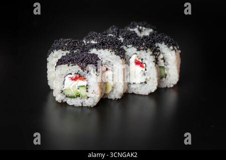 Rouleaux de sushi disposés soigneusement sur une surface noire. Les rouleaux sont recouverts de graines de sésame noir et contiennent du fromage à la crème, du concombre et du poisson rouge. Banque D'Images