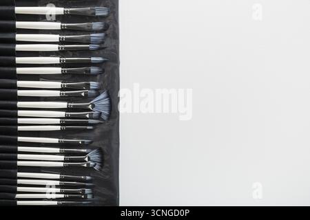 Pinceaux, couteaux de palette dans un étui à crayons sur fond de toile blanche. Gros plan Banque D'Images