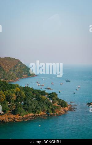 Vue panoramique sur la côte avec collines verdoyantes, rivage rocheux et bateaux de pêche colorés flottant sur la mer bleue calme sous un ciel clair Banque D'Images