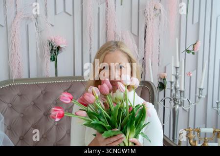 Une femme élégante tenant des tulipes roses dans un environnement intérieur magnifiquement stylisé avec charme et sophistication Banque D'Images