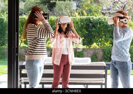 Diverses amies féminines debout sur un patio couvert avec banc portant des casques vr ajustables Banque D'Images
