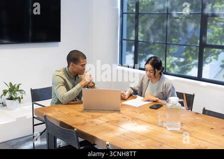Divers collègues annotent le document avec un stylo à la table de réunion du bureau, ordinateur portable et smartphone Banque D'Images