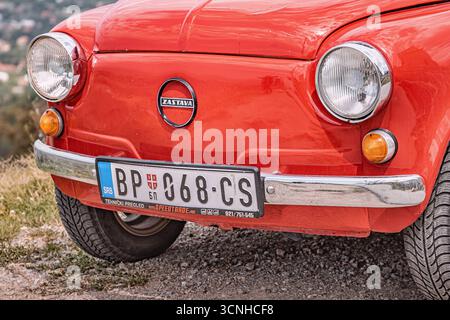 3 août 2025, Vrsac, Serbie : gros plan d'une Zastava 750 rouge brillant, une voiture serbe classique, garée sur une route de gravier, soulignant son charme vintage Banque D'Images