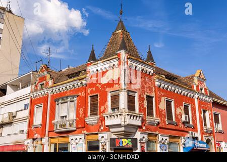 3 août 2025, Vrsac, Serbie : vue en angle bas d'un vieux bâtiment rouge délabré avec de petites tourelles, de la peinture écaillée et des volets fermés Banque D'Images
