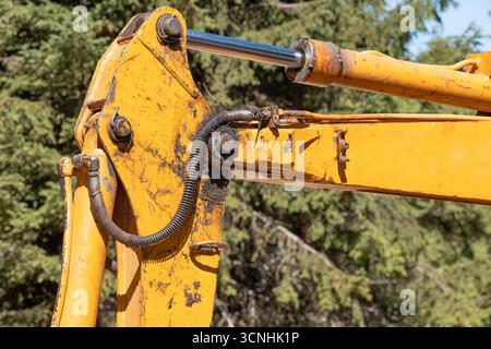 Bras de pelle jaune doté d'un piston et d'un cylindre hydrauliques, montrant l'usure due à une utilisation industrielle lourde dans un environnement extérieur naturel Banque D'Images