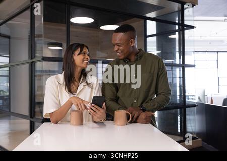 Divers collègues pointant le smartphone, s'appuyant sur le comptoir blanc dans la zone de pause du bureau Banque D'Images