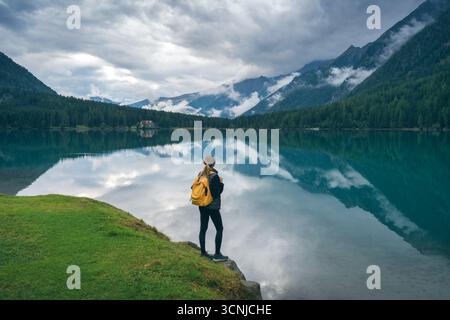 Femme avec sac à dos jaune debout près du lac dans les montagnes Banque D'Images