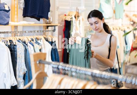 La cliente fille choisit un chemisier dans le magasin de marque Banque D'Images