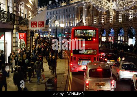 LONDRES, ROYAUME-UNI. 17 DÉCEMBRE 2016. Les clients se rassemblent à l'extérieur des magasins sous les lumières de Noël de Regent Street tandis qu'un bus à impériale rouge passe. Banque D'Images