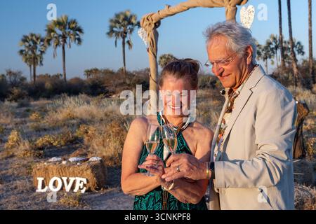 Couple de mariage toast champange lors d'une cérémonie de mariage en plein air dans la forêt de palmiers Makalani - réserve naturelle d'Onguma, Namibie, Afrique Banque D'Images