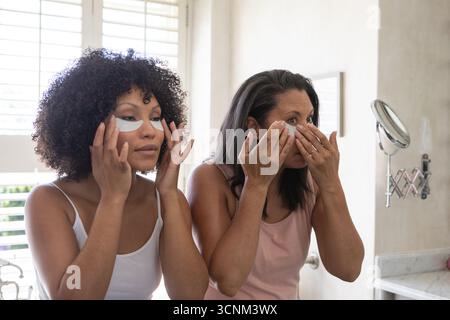 La mère et la fille placent des patchs de gel sous les yeux dans la salle de bains de la vanité de la maison avec comptoir en marbre Banque D'Images