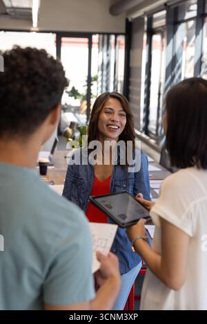 Divers collègues discutent du plan de projet autour d'un long bureau avec tablette, documents, café Banque D'Images