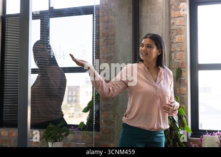 Femme debout dans un chemisier rose pointant vers la carte sur un panneau de verre avec marqueur dans le bureau Banque D'Images