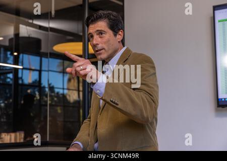 Homme faisant des gestes et présentant une feuille de calcul par un mur de verre dans la salle de réunion sous une lumière circulaire Banque D'Images