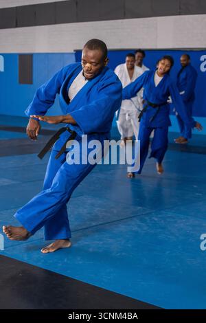 Divers étudiants de dojo dans les ceintures sig suivant un instructeur afro-américain marchant sur des tapis Banque D'Images