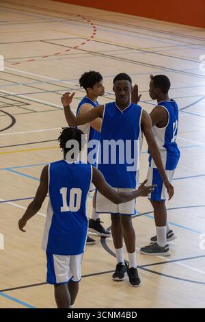 Divers coéquipiers masculins donnant des high-fves sur le terrain de gymnastique portant des maillots bleus et de basket-ball Banque D'Images
