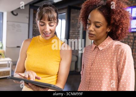 Diverses collègues féminines examinent les détails du projet sur tablette au bureau avec tableau blanc Banque D'Images