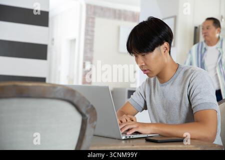 Père asiatique avec fils à l'aide d'un ordinateur portable avec smartphone à la table à manger dans la cuisine à la maison, espace de copie Banque D'Images