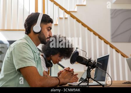 Divers co-hôtes enregistrant un épisode de podcast dans le home studio avec microphone et ordinateurs portables Banque D'Images