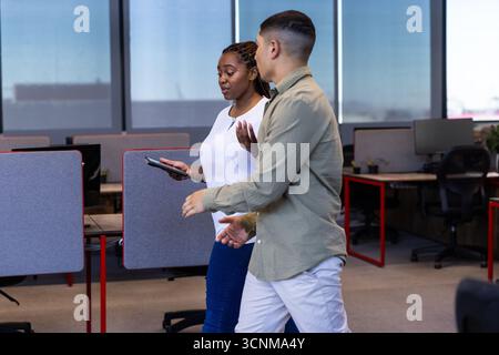 Divers collègues marchant dans un bureau ouvert parlant, tenant une tablette près des écrans d'ordinateur Banque D'Images