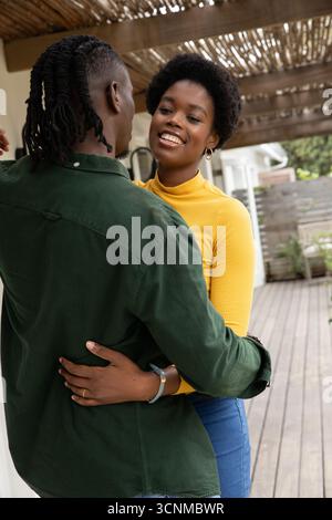 Couple afro-américain adulte moyen embrassant sur le pont sous la pergola avec clôture, plantes en pot Banque D'Images