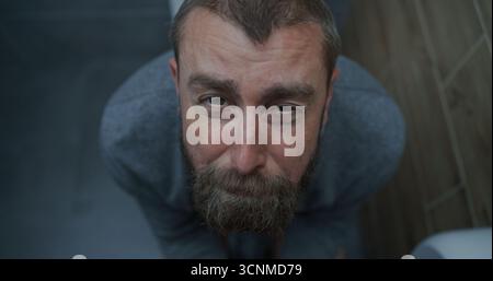 Vue de dessus sur l'homme avec l'expression faciale tendue assis sur les toilettes, souffrant de diarrhée, estomac Ache. Homme d'affaires éprouvant l'inconfort digestif et l'indigestion dans les toilettes pendant le travail au bureau. Banque D'Images