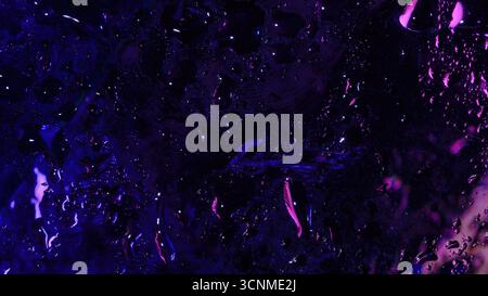 Plan macro abstrait de verre mouillé avec des reflets violets et violets profonds au néon, avec des gouttelettes d'eau dispersées et des traces de liquide. Banque D'Images
